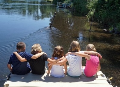 Image of children sat on the deck by the river with their arms around each other
